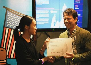 Person presenting an award certificate to a student, shaking hanks.